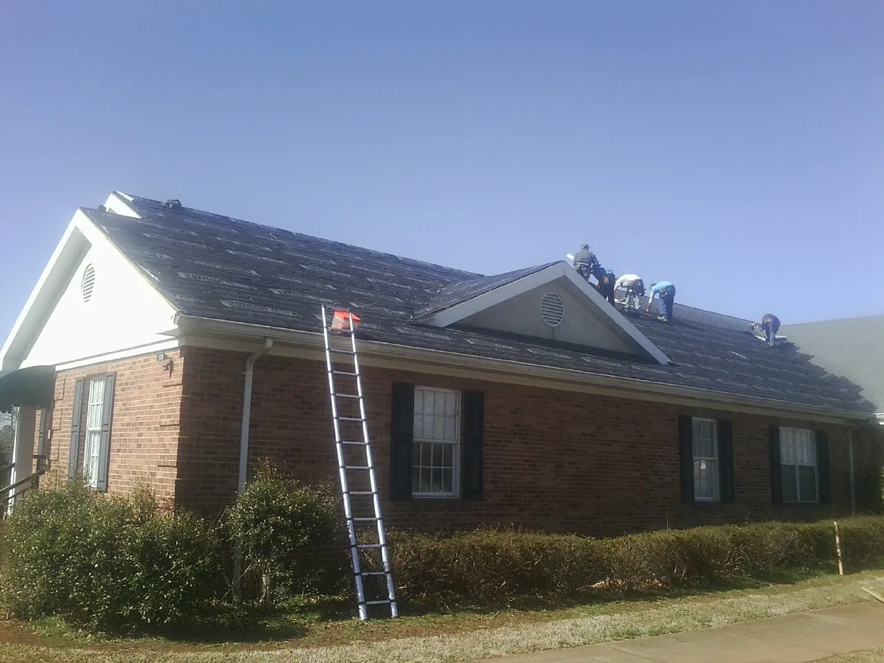 Crew tearing shingles off a brick ranch roof with a ladder set — Metal Roof Repair work by our crew in Belfair