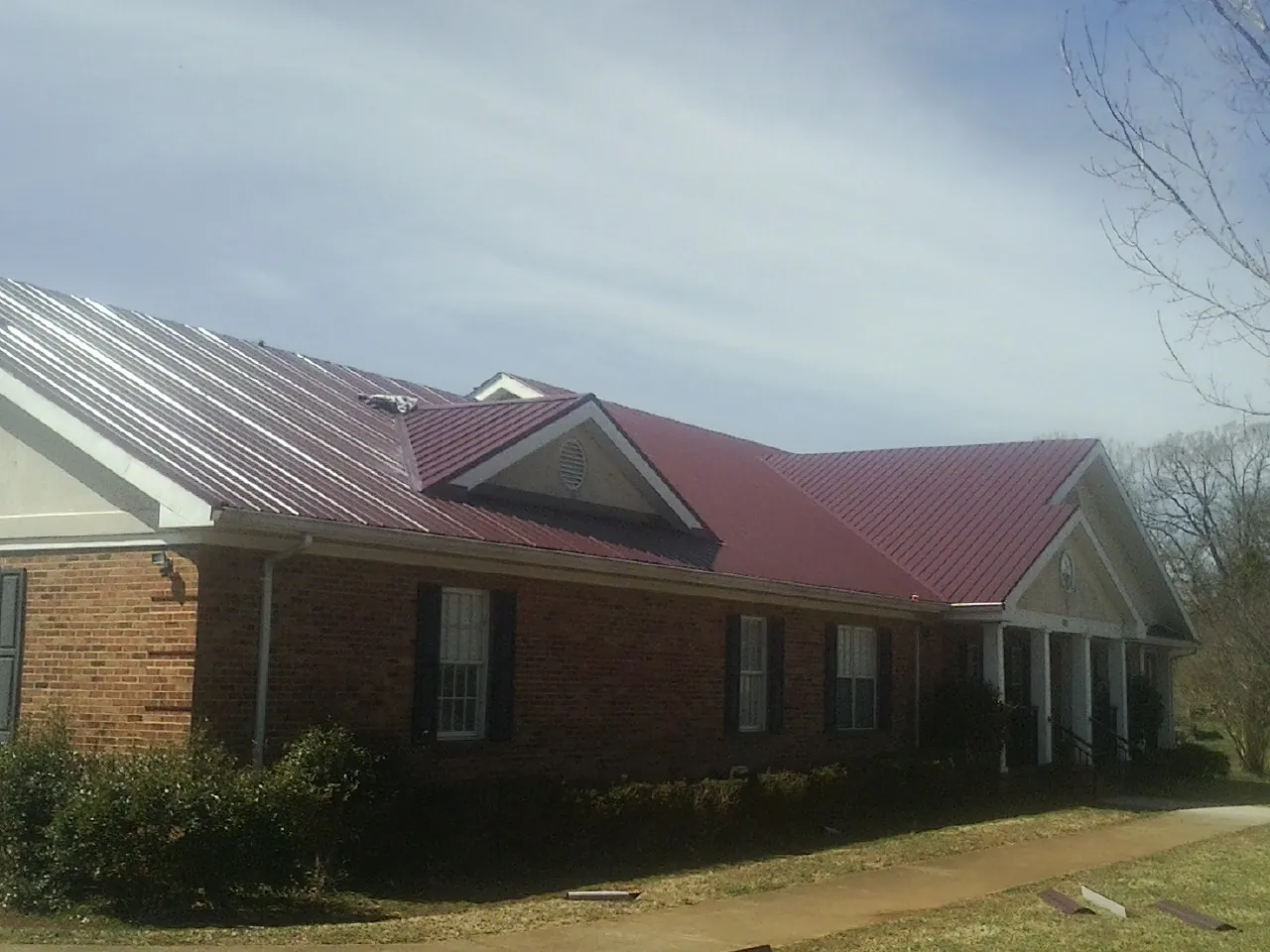Red metal roof with gabled entries on a long brick building, from a Hail Damage Roof Repair job in Belfair