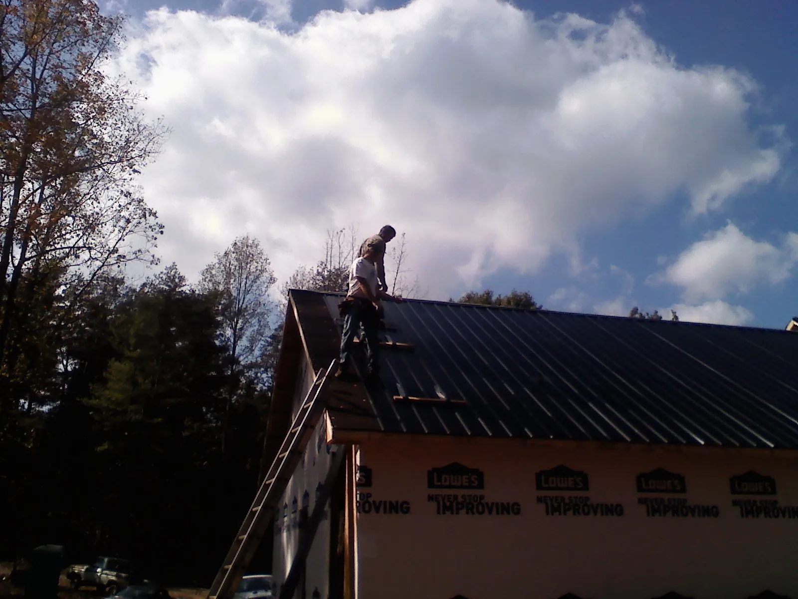Roofer fastening dark metal panels high against a cloudy sky, from a Roof Inspection job in Belfair